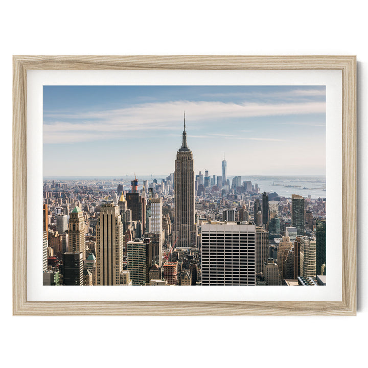 The image is a panoramic view of the New York City skyline, showcasing the iconic Empire State Building and other skyscrapers against a clear blue sky.