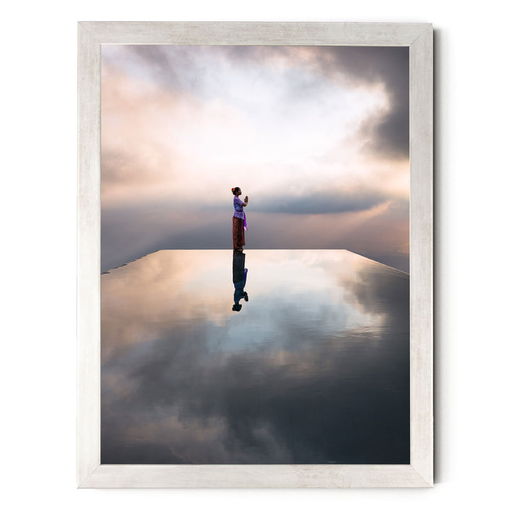 A person stands on a reflective surface, gazing out at the horizon where the sky meets the clouds, creating a serene and contemplative scene.