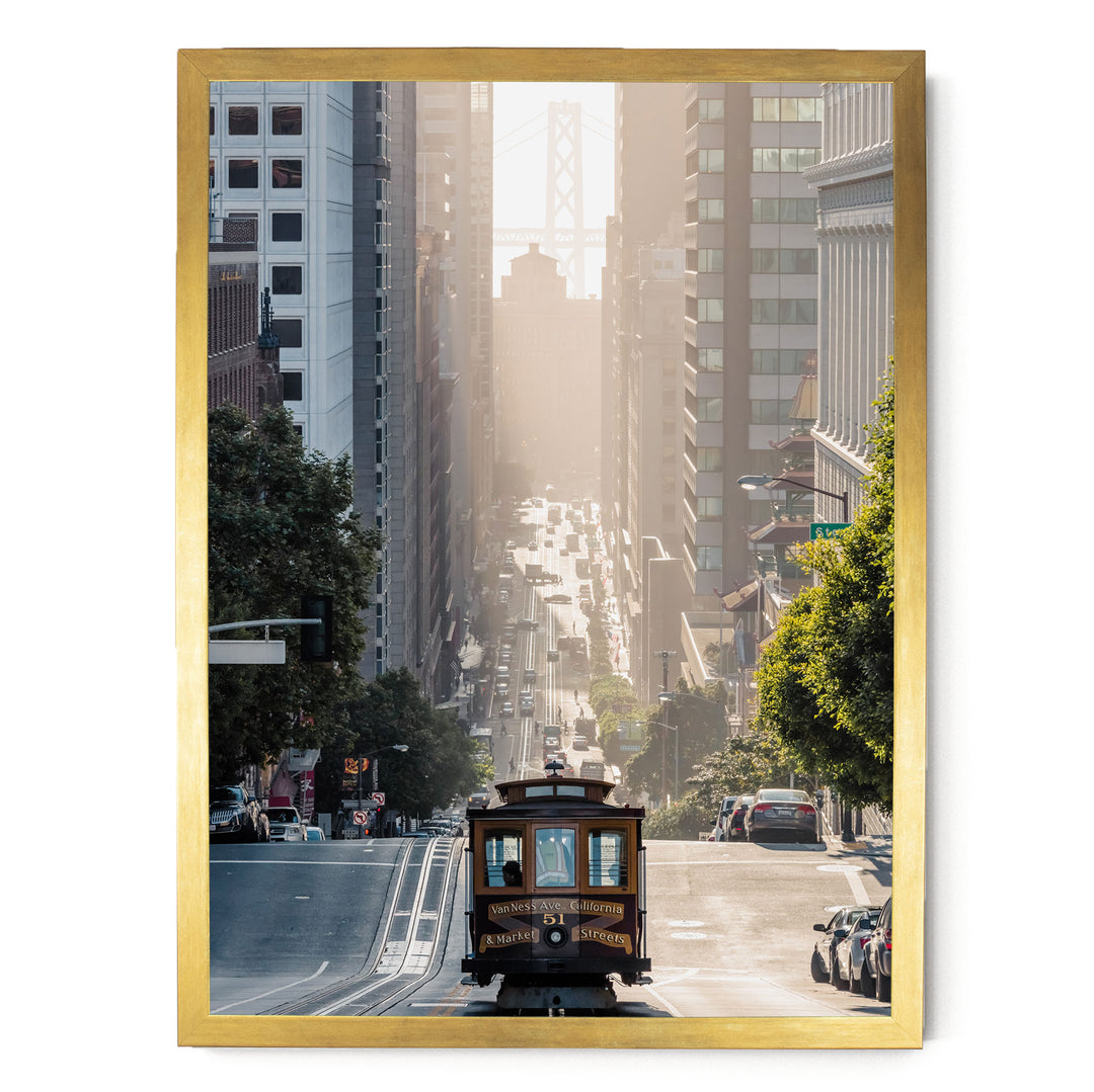 A framed photograph depicting a trolley car traveling down a busy street in San Francisco, with tall buildings and a bridge in the background.