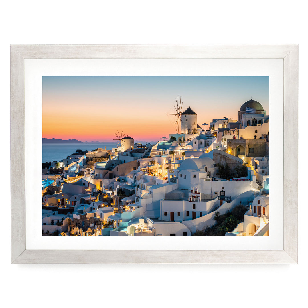a picturesque coastal town in the Greek island of Santorini, with its iconic windmills and buildings illuminated against the backdrop of a stunning sunset.