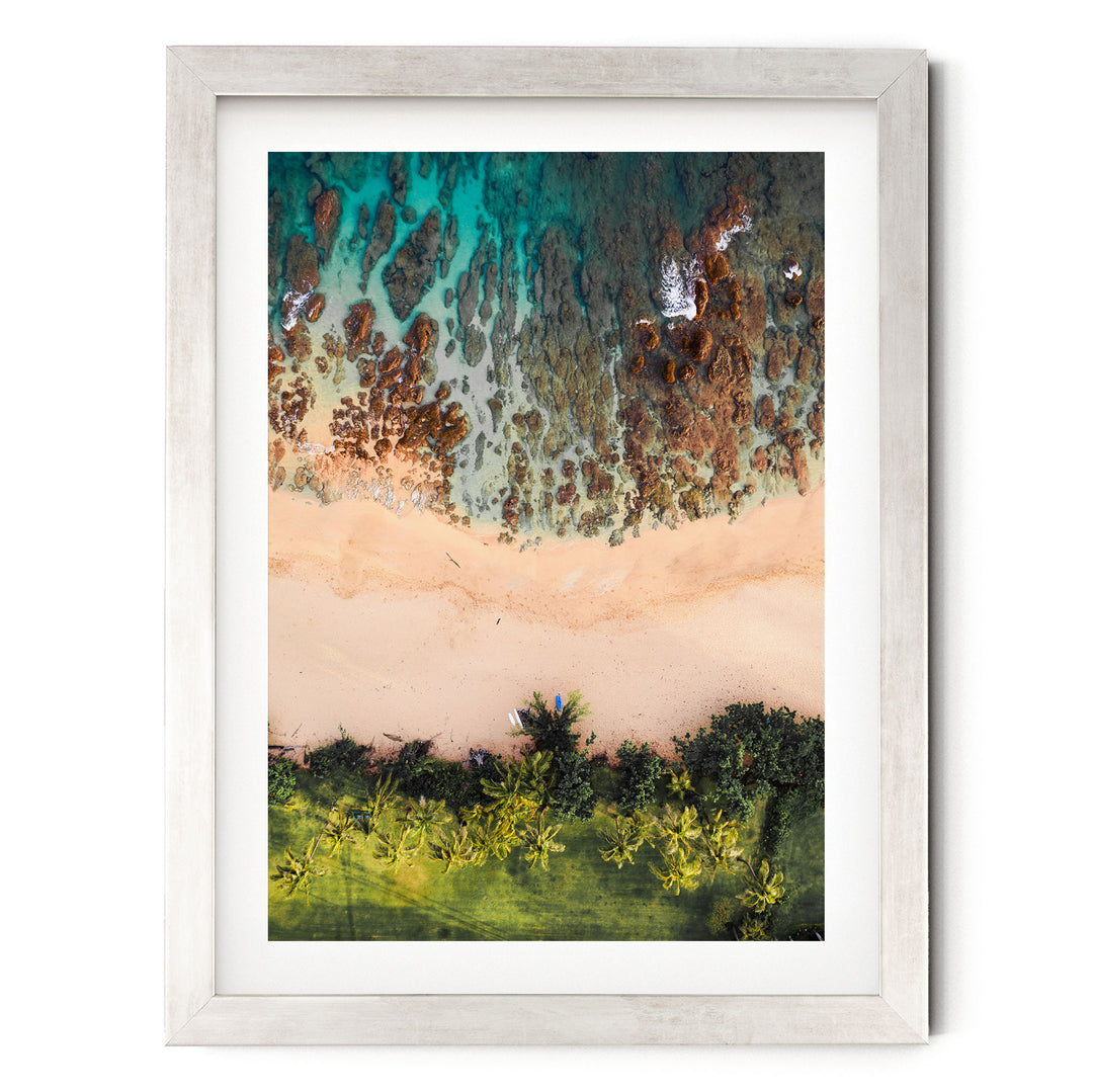The image is a framed aerial view of a beach with a clear blue sky, palm trees, and a sandy shoreline.