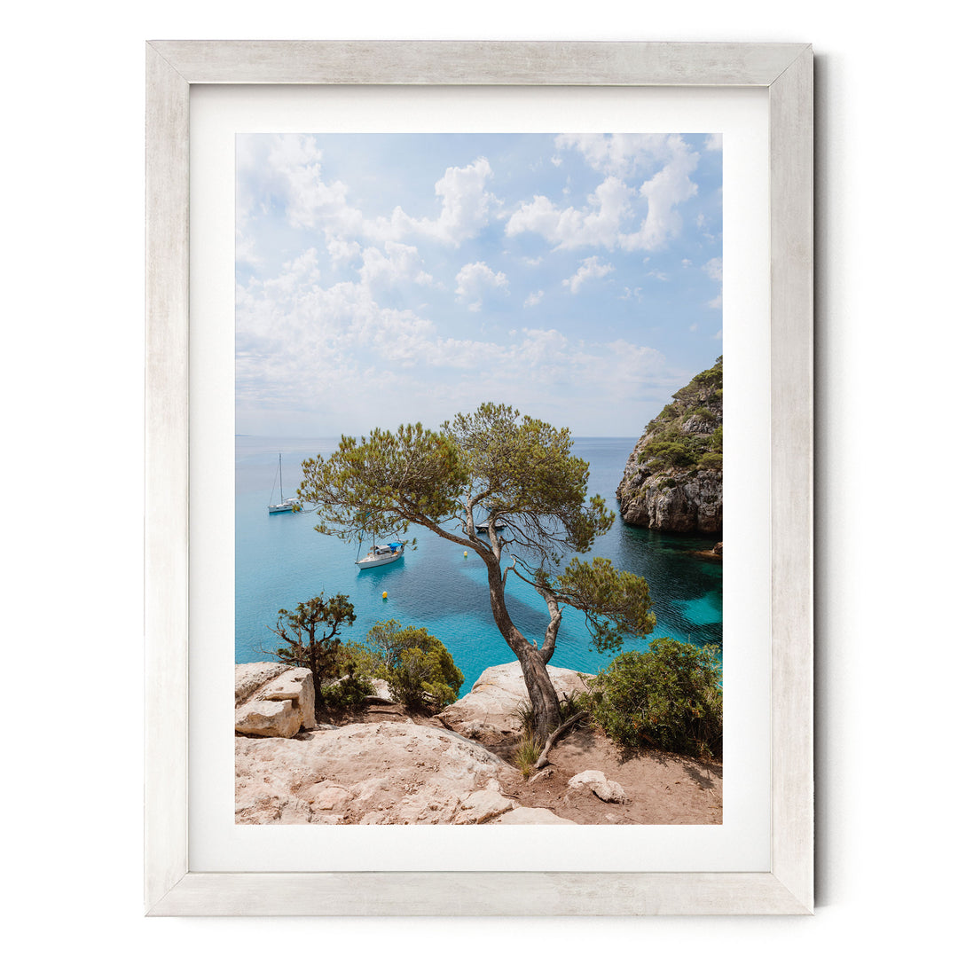 a serene coastal landscape with a rocky cliff overlooking a turquoise sea dotted with boats.