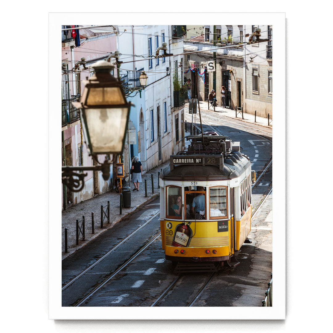 A yellow tram is traveling down a street lined with buildings and a lamp post.