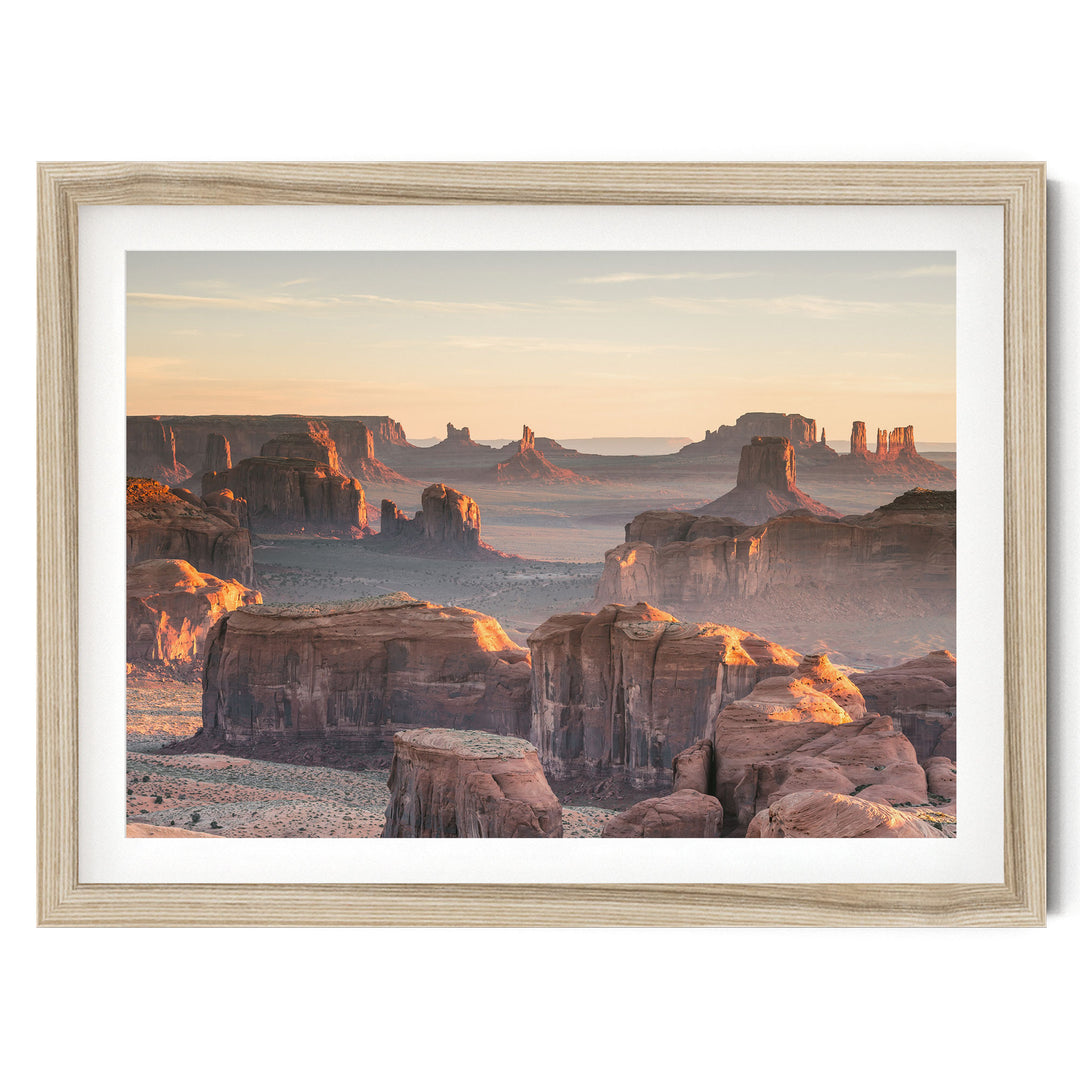 a breathtaking view of the Grand Canyon, with its towering red rock formations bathed in the warm glow of the setting sun. The sky above is a beautiful shade of orange, creating a stunning backdrop for the natural landscape. The photograph is framed and appears to be a piece of art, showcasing the beauty and grandeur of this iconic landmark.