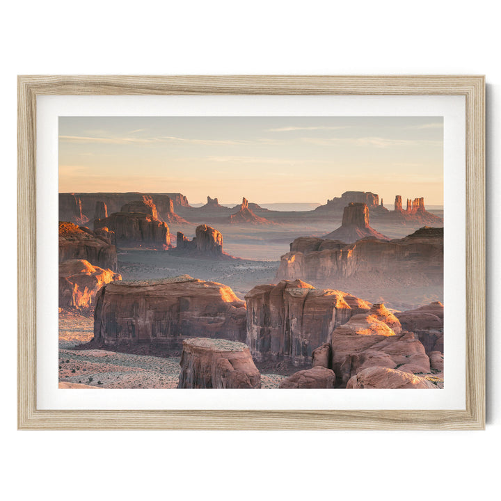 a breathtaking view of the Grand Canyon, with its towering red rock formations bathed in the warm glow of the setting sun. The sky above is a beautiful shade of orange, creating a stunning backdrop for the natural landscape. The photograph is framed and appears to be a piece of art, showcasing the beauty and grandeur of this iconic landmark.
