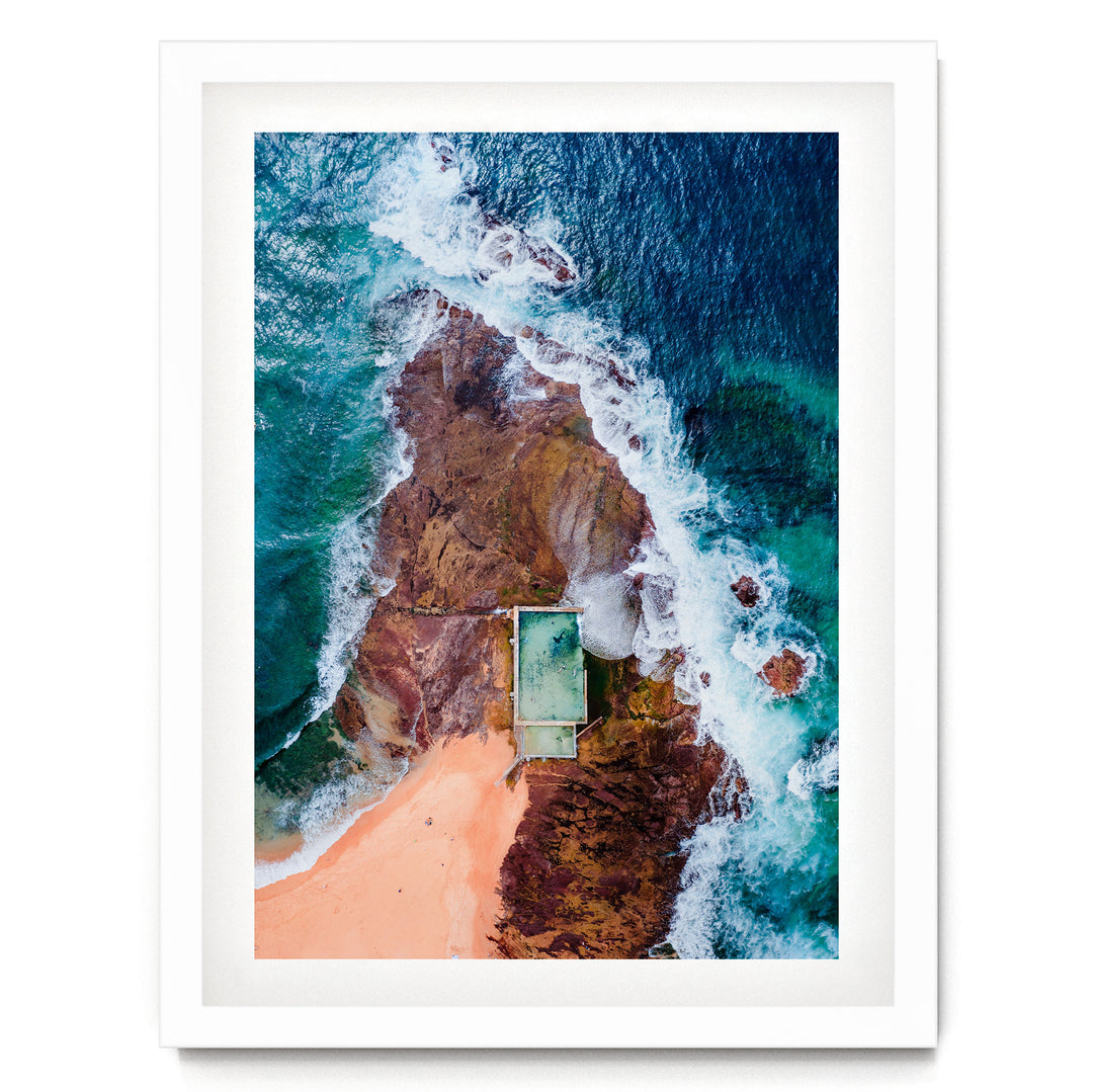 An aerial view of a beach with a swimming pool, surrounded by rocky cliffs and crashing waves.