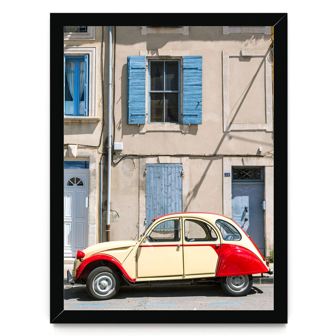 A vintage yellow and red car is parked in front of a building with blue shutters and a white door.