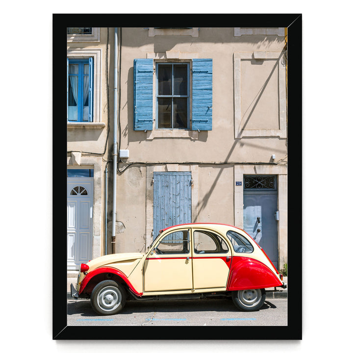 A vintage yellow and red car is parked in front of a building with blue shutters and a white door.