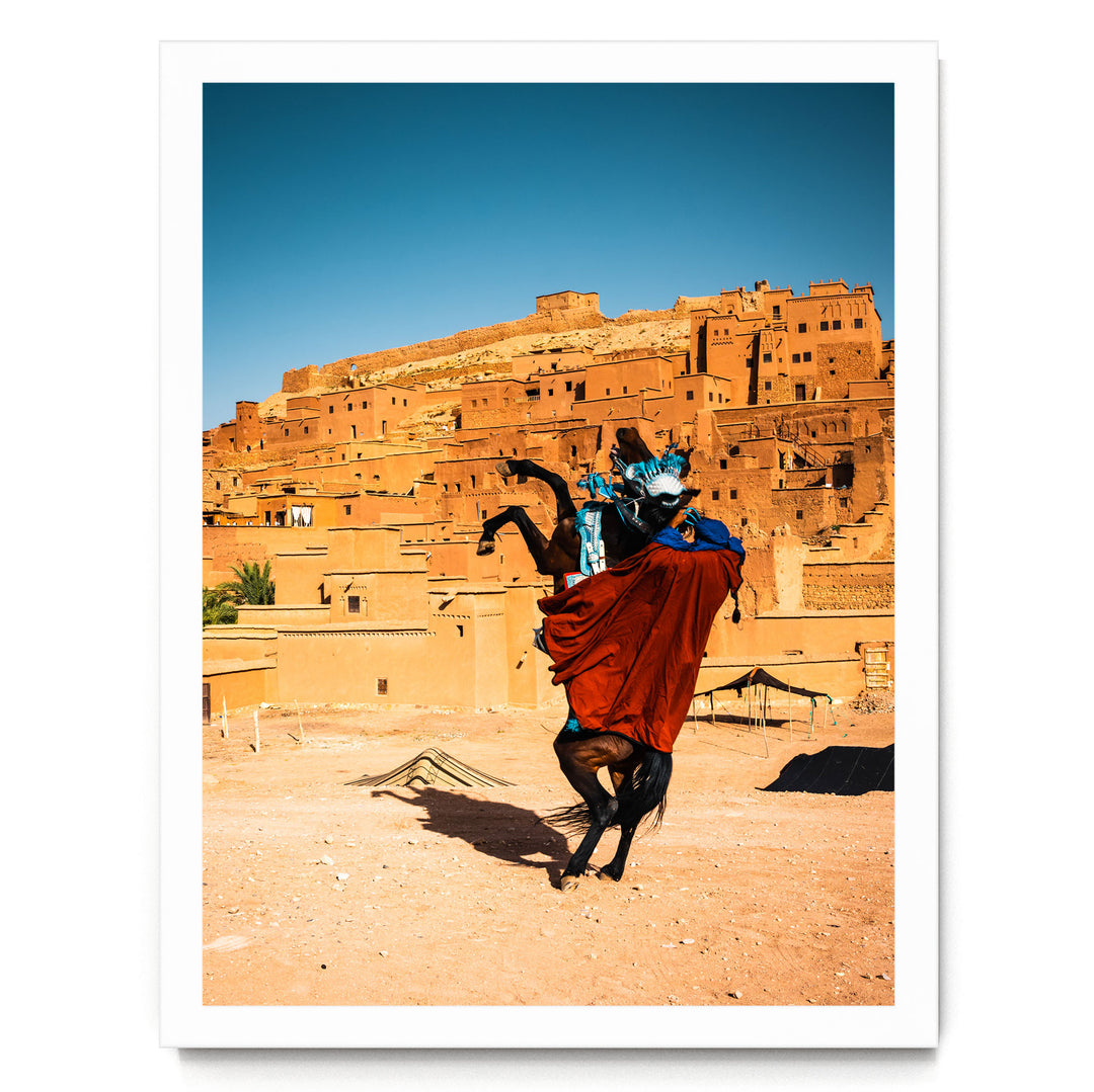 A person riding a horse in a desert-like setting, with a large, multi-story structure in the background.