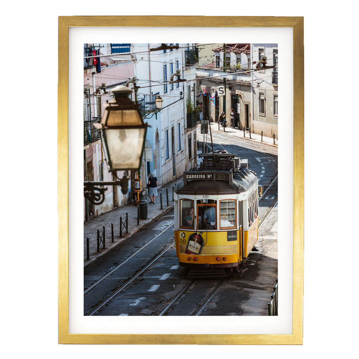 A yellow tram is traveling down a street lined with buildings and lampposts in an urban setting.