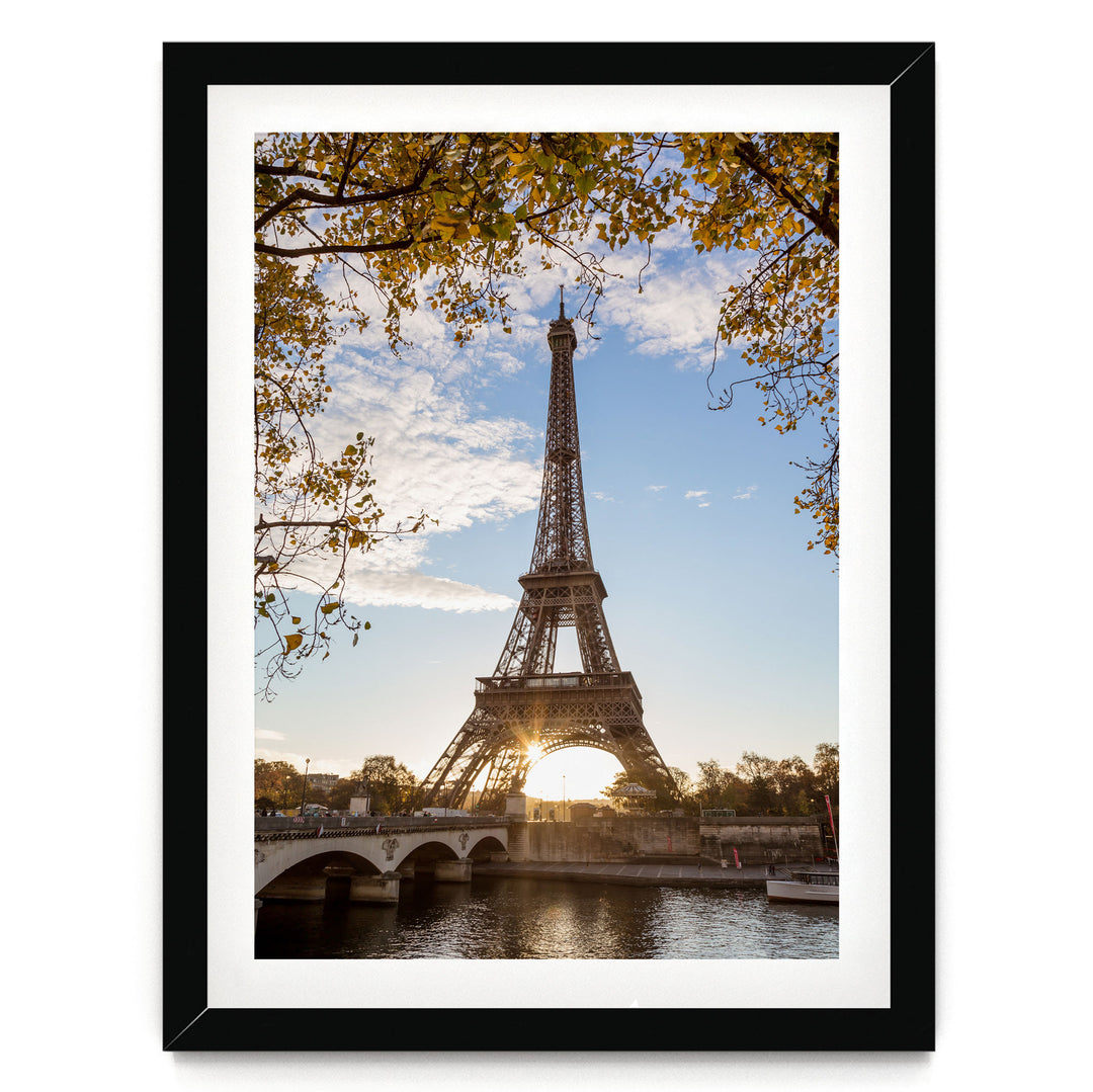 the Eiffel Tower in Paris, France, with a bridge and trees in the foreground, and the sun setting behind the tower.