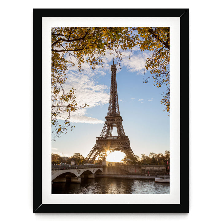 the Eiffel Tower in Paris, France, with a bridge and trees in the foreground, and the sun setting behind the tower.