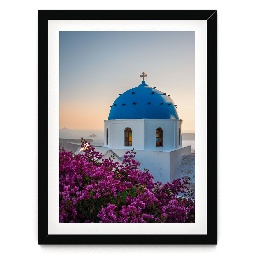 A framed photograph of a blue domed church with a cross on top, surrounded by a field of pink flowers.