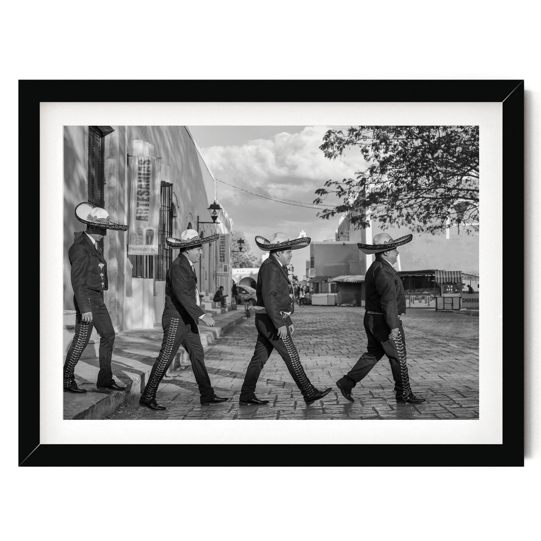 A black and white photograph of four men wearing sombreros walking down a street.