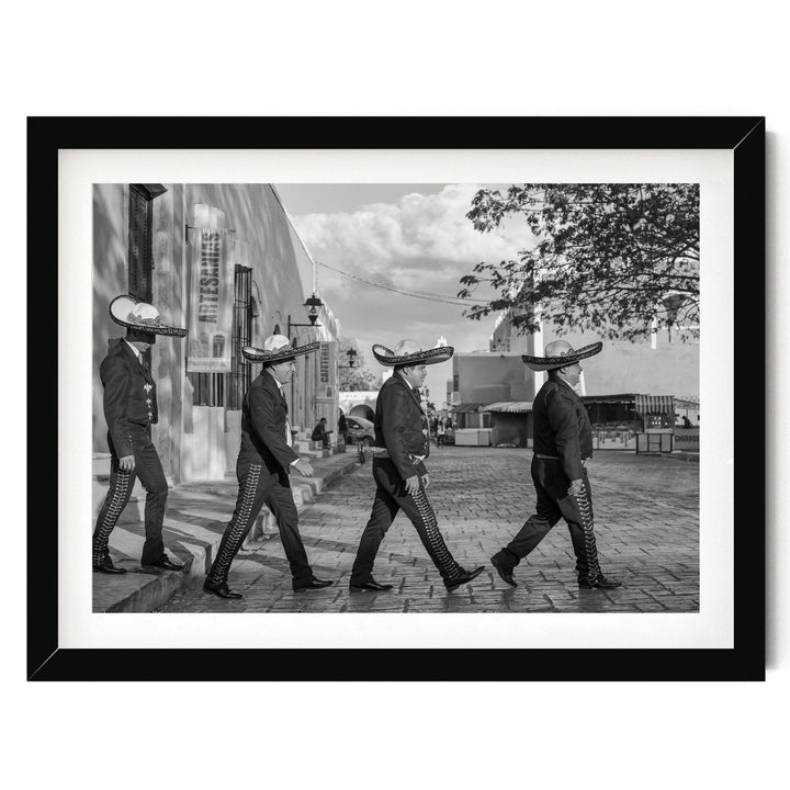 A black and white photograph of four men wearing sombreros walking down a street.