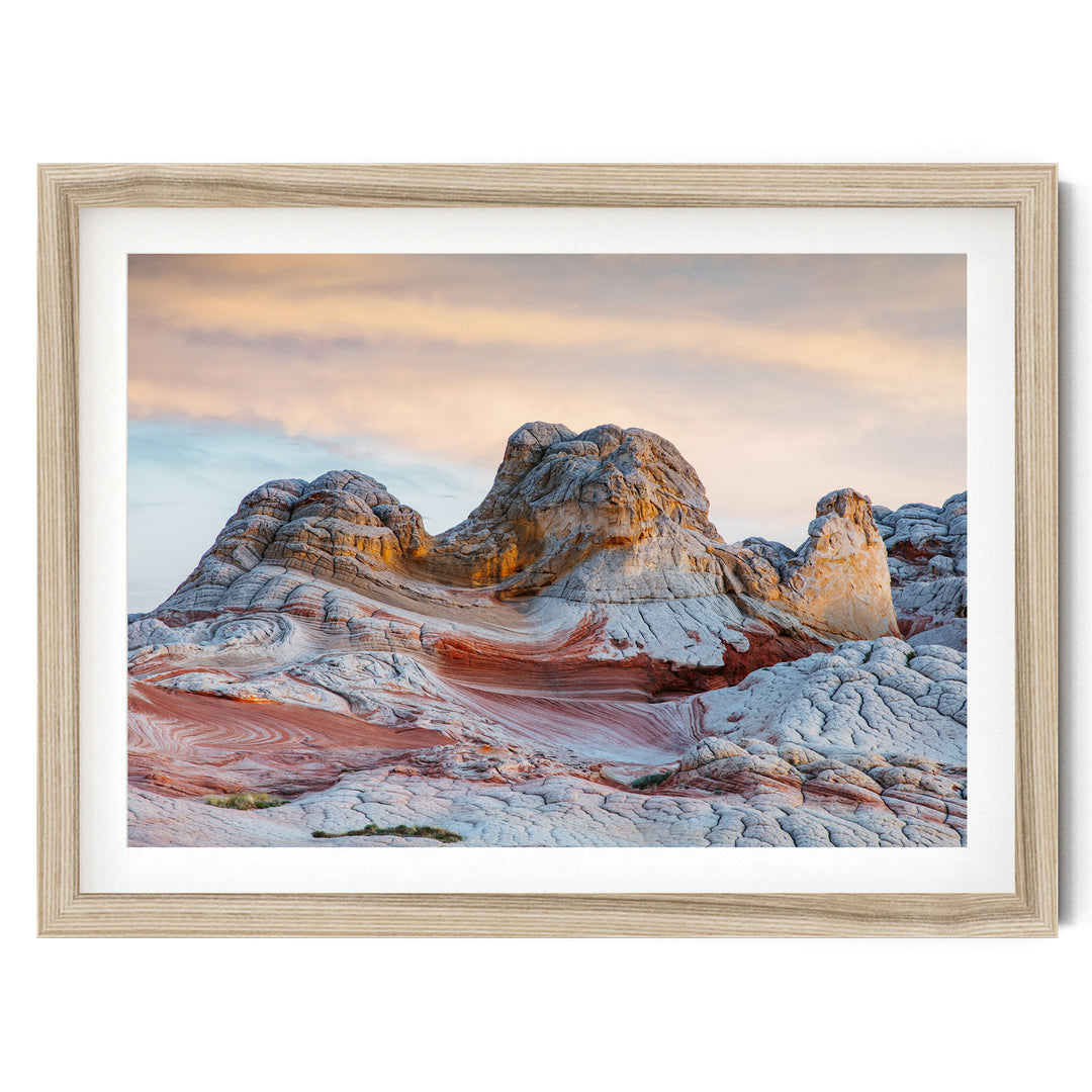a striking natural landscape with a large, multi-layered rock formation in the foreground, set against a vibrant sky with a gradient of orange and pink hues.