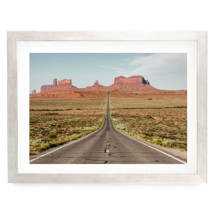 A long, straight road stretches out into the distance, leading towards a majestic mountain range in the background.
