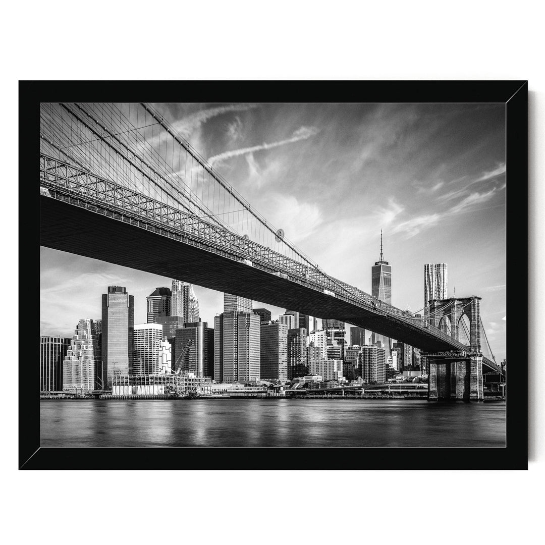 A black and white photograph of the Brooklyn Bridge spanning the East River, with the New York City skyline visible in the background.