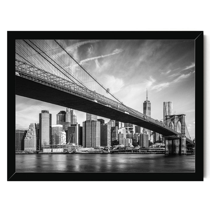 A black and white photograph of the Brooklyn Bridge spanning the East River, with the New York City skyline visible in the background.