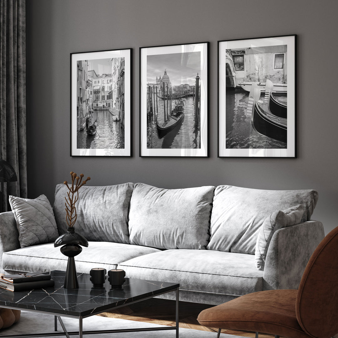 a modern living room with a gray sofa, a black coffee table, and three framed black and white photographs of Venice canal scenes hanging on the wall above the sofa.