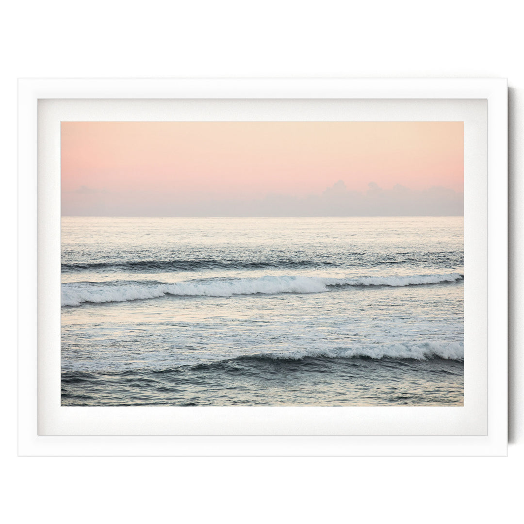 A serene ocean scene with waves gently lapping against the shore, set against a soft pink and orange sky.