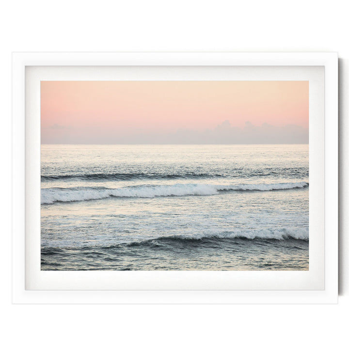 A serene ocean scene with waves gently lapping against the shore, set against a soft pink and orange sky.
