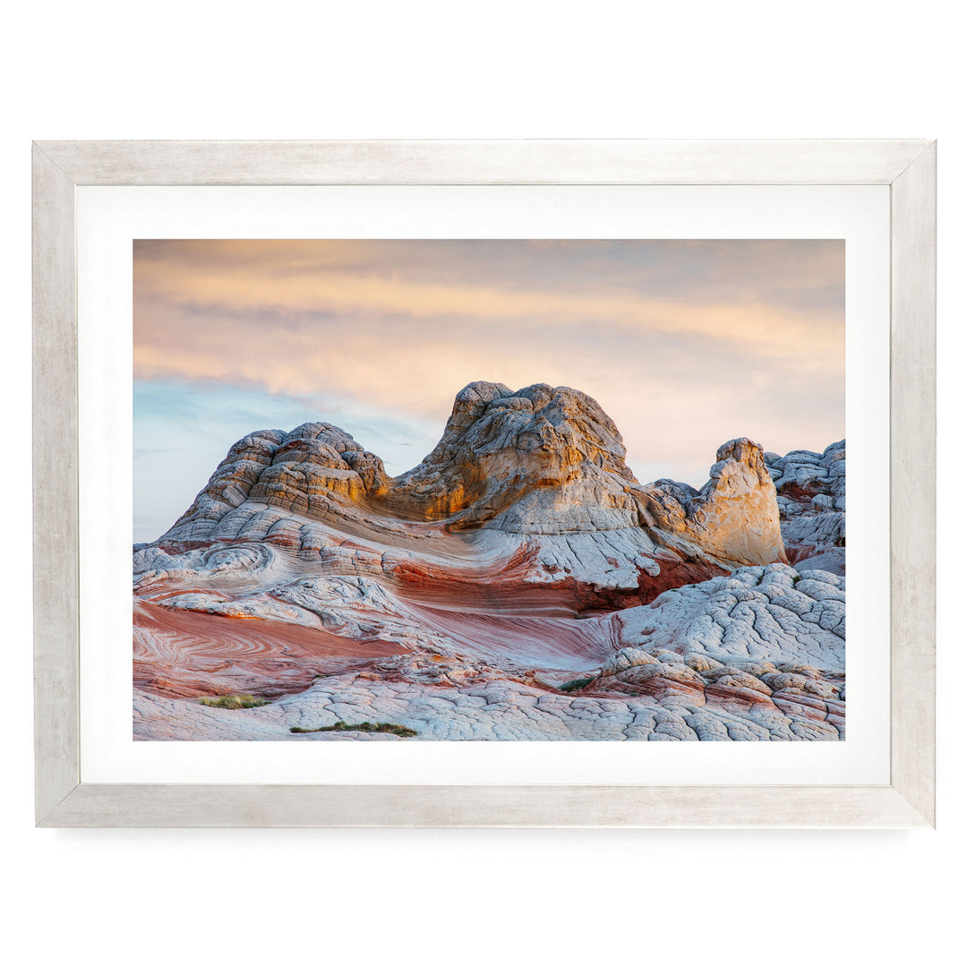 a striking natural landscape with a large, multi-layered rock formation in the foreground, set against a vibrant sky with a gradient of orange and pink hues.