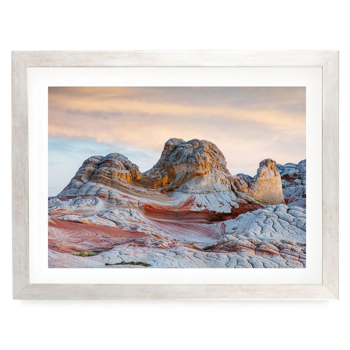 a striking natural landscape with a large, multi-layered rock formation in the foreground, set against a vibrant sky with a gradient of orange and pink hues.