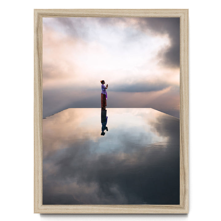 A person stands on a reflective surface, gazing out at the sky, with clouds and a sunset in the background.