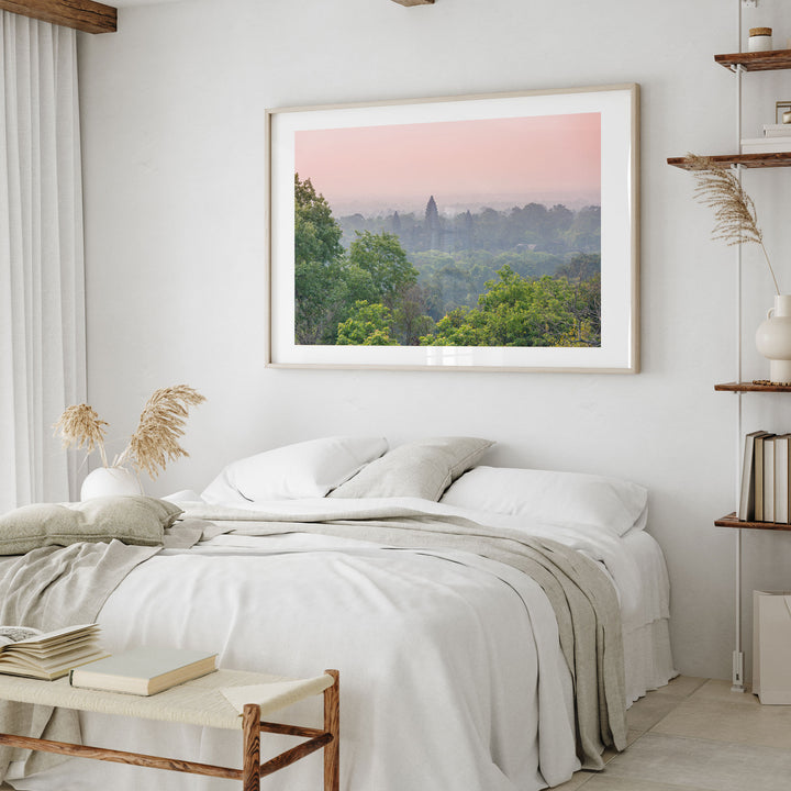 a serene bedroom scene with a large framed landscape photograph hanging on the wall above a bed with white linens and a gray throw blanket.