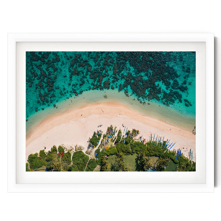 The image is an aerial view of a tropical beach with crystal clear turquoise waters, sandy shores, lush vegetation, and several boats on the water.