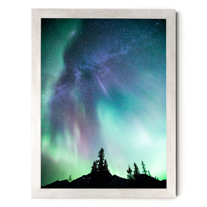 a stunning night sky with a vibrant display of the Aurora Borealis, or Northern Lights, illuminating the surrounding landscape. The silhouettes of trees can be seen in the foreground, adding a sense of depth and scale to the scene. The colors in the image are predominantly green, blue, and purple, creating a captivating and otherworldly atmosphere.