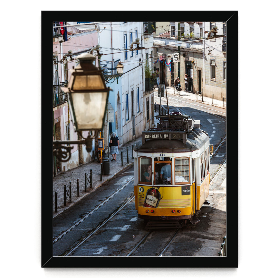 A yellow tram is traveling down a street lined with buildings and a street lamp.