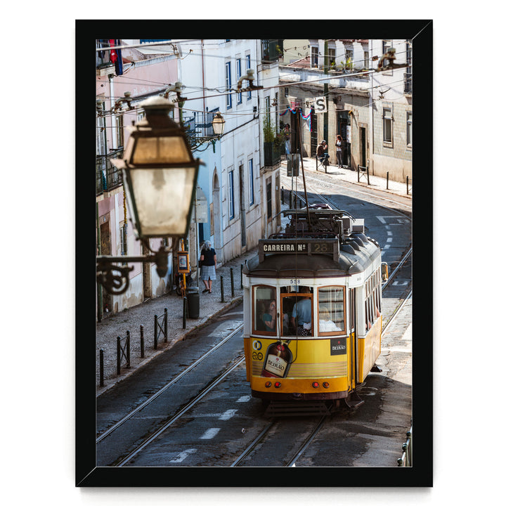 A yellow tram is traveling down a street lined with buildings and a street lamp.