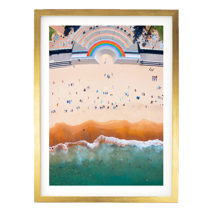 The image is an aerial view of a beach with a large rainbow arching over the top of a building, creating a vibrant and colorful scene.