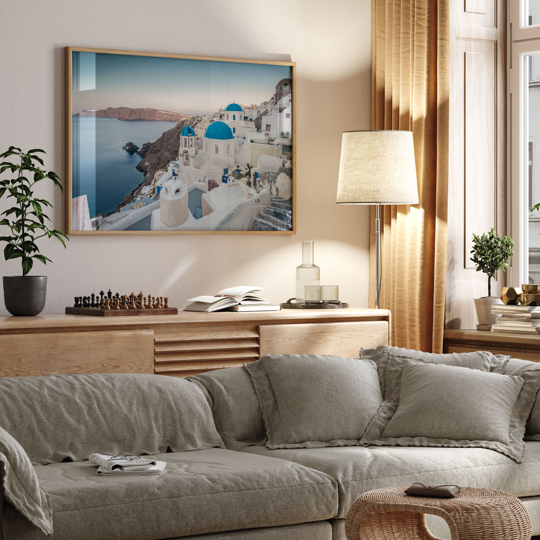 a cozy living room with a large framed picture of a picturesque Greek island, a comfortable gray sofa, and a wooden side table with a lamp.