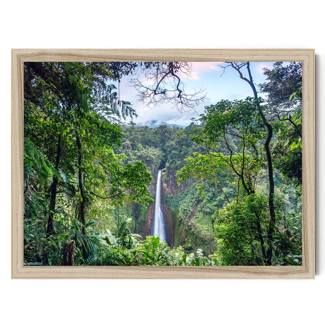 A lush, verdant forest with a towering waterfall cascading down the rocky cliff face, framed in a wooden frame.