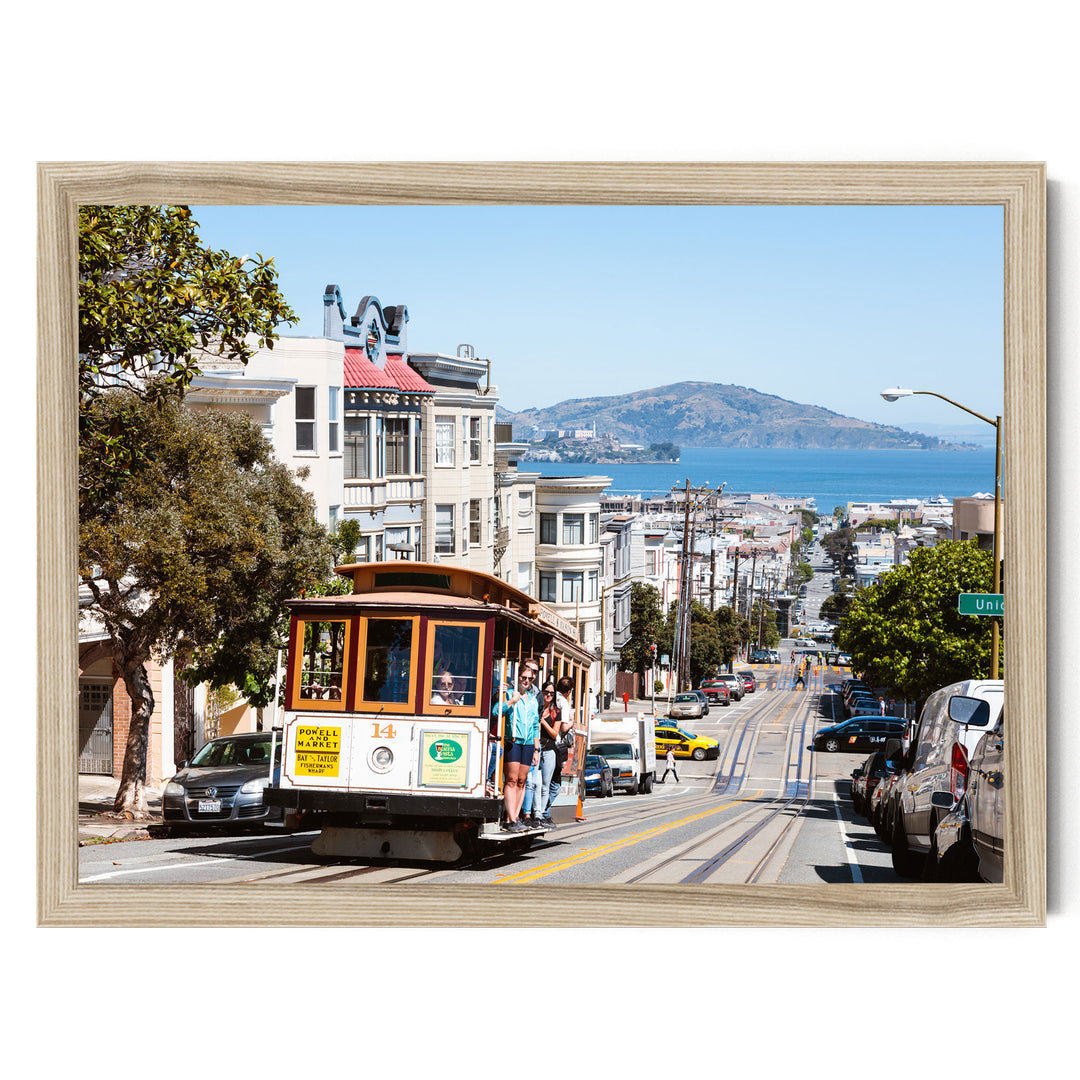 A cable car is traveling down a busy street in San Francisco, with buildings, cars, and pedestrians visible in the background.