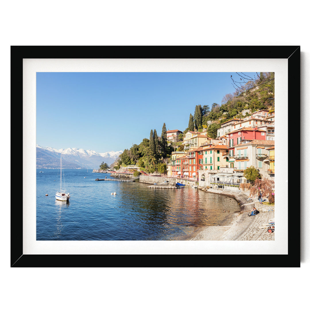 A picturesque coastal town with colorful buildings, a calm lake, and a sailboat on the water.