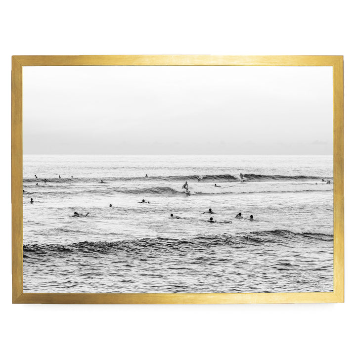 A black and white photograph of a group of people swimming and surfing in the ocean, with waves visible in the background.