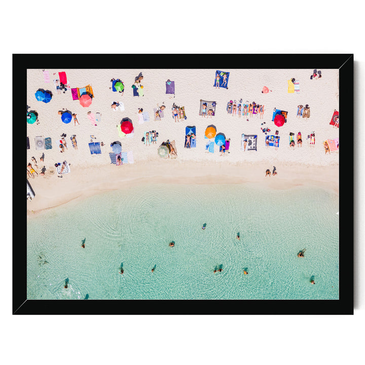 a crowded beach with numerous people enjoying the sunny day, some swimming in the clear blue water, and colorful umbrellas providing shade.