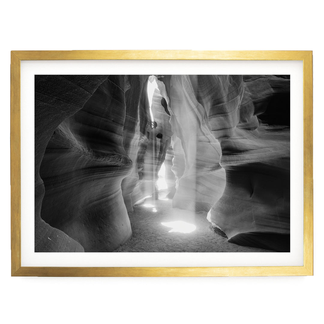 A black and white photograph of a narrow passage in a rock formation, with light shining through the opening and creating a dramatic effect.