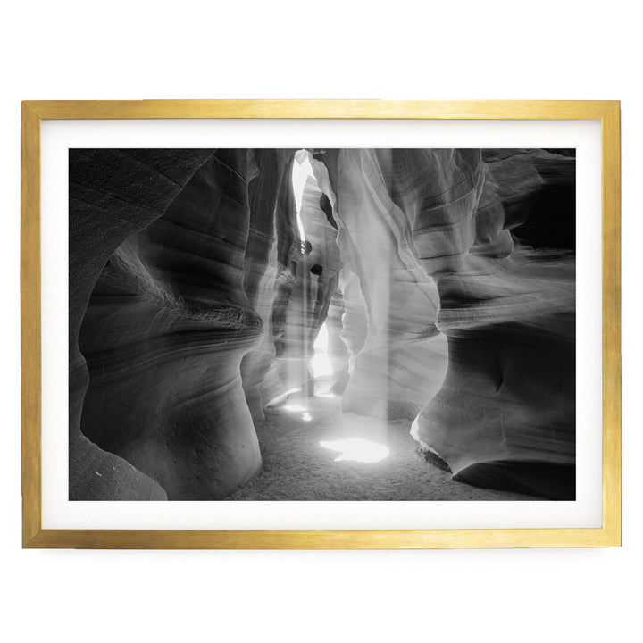 A black and white photograph of a narrow passage in a rock formation, with light shining through the opening and creating a dramatic effect.