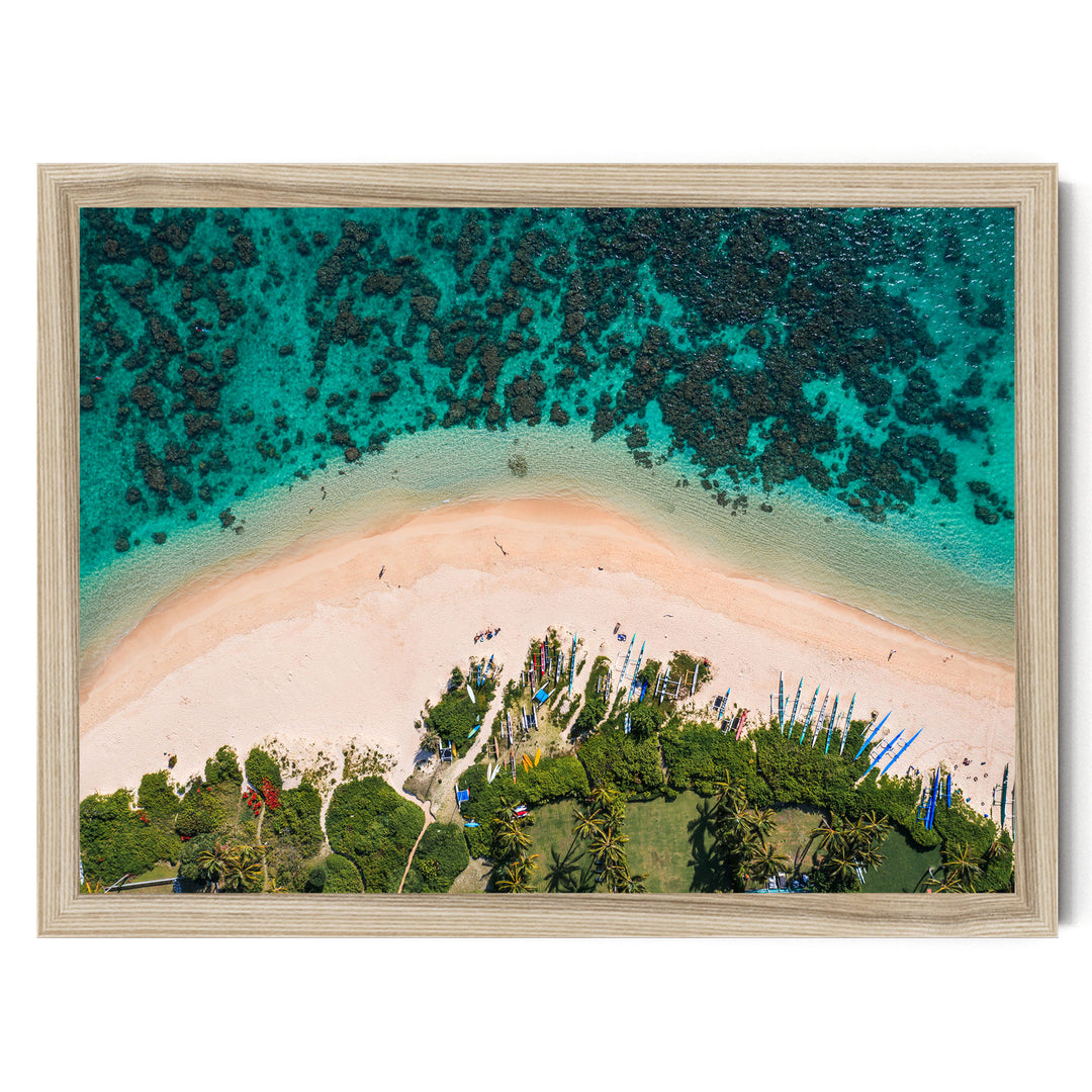The image is an aerial view of a tropical beach with crystal clear turquoise waters, sandy shores, and lush vegetation surrounding the area.