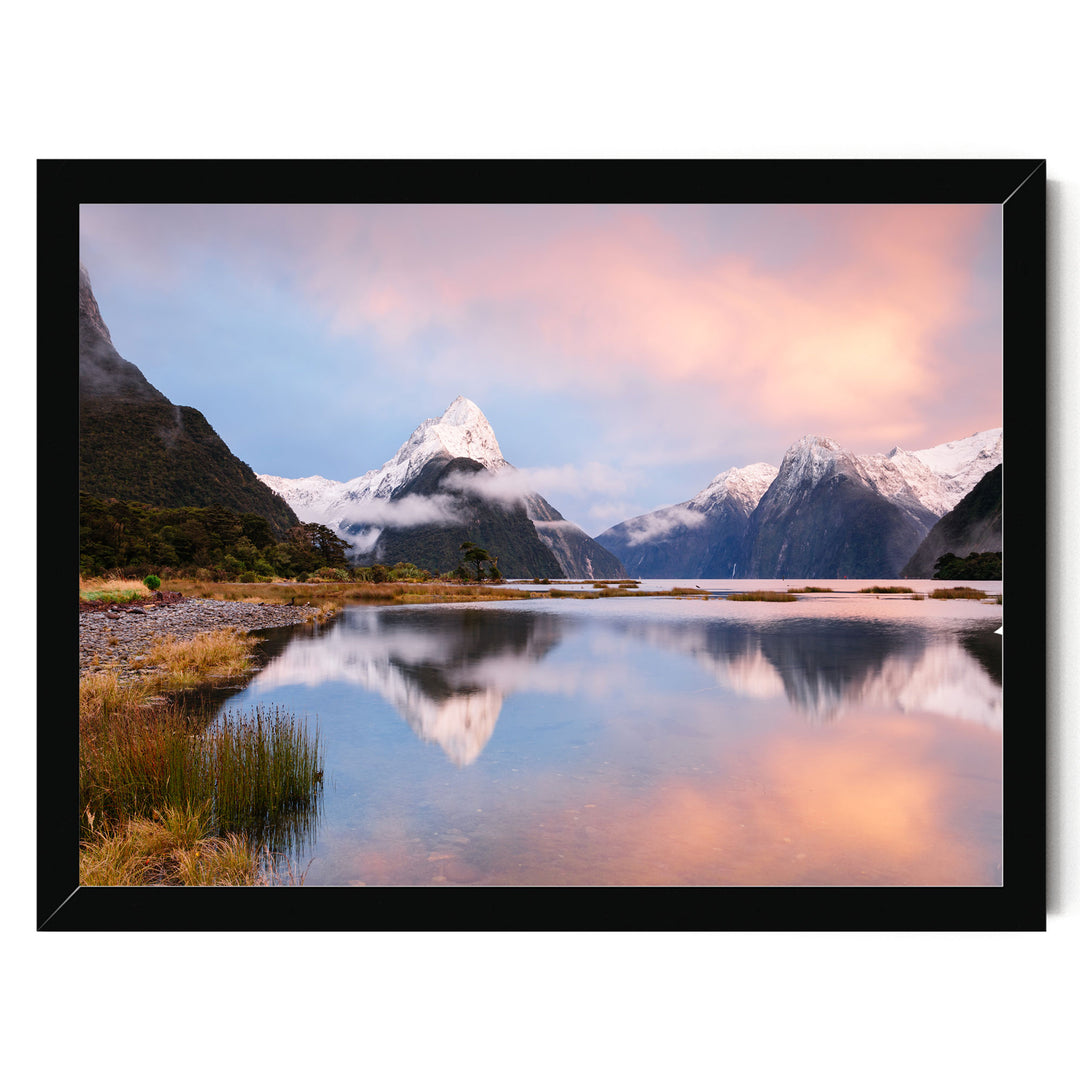 A breathtaking landscape featuring a serene lake surrounded by majestic snow-capped mountains, with the mountains' peaks reflected in the calm waters. The sky is painted in a beautiful gradient of pink and orange, creating a stunning backdrop for the scene.