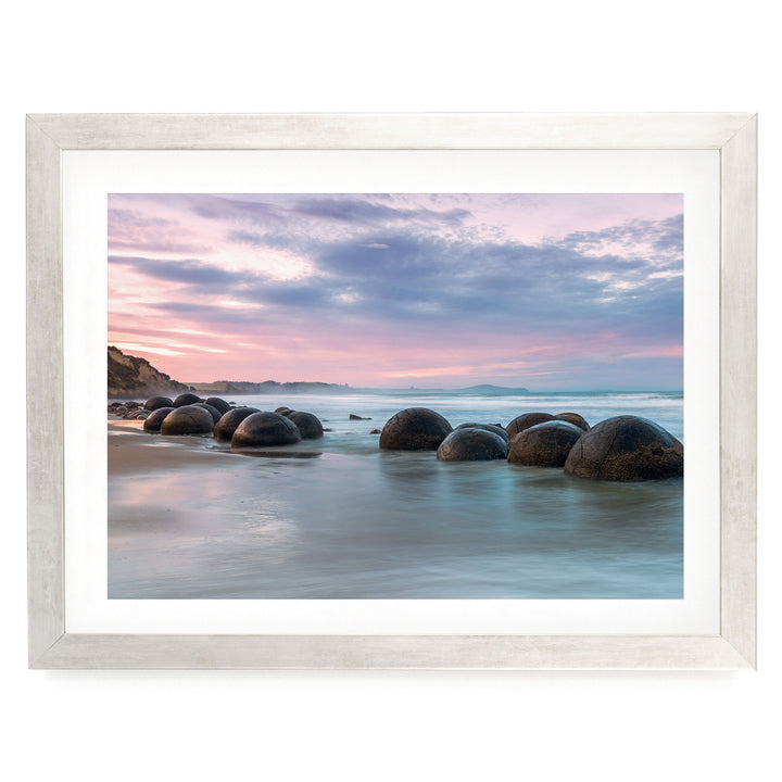 A serene beach scene with a collection of large, round boulders in the water, set against a picturesque sunset sky.
