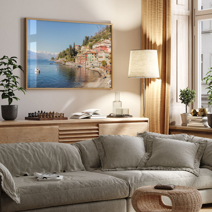 a cozy living room with a large framed picture of a coastal town hanging on the wall, a comfortable gray sofa, a wooden side table with a lamp, and various decorative elements such as potted plants and books.
