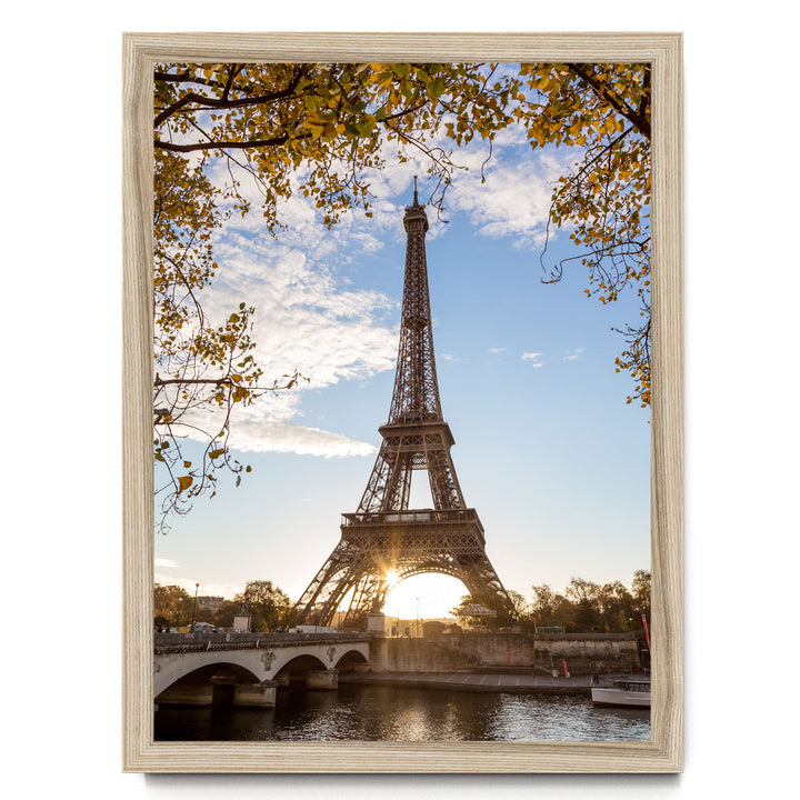 the Eiffel Tower in Paris, France, with a bridge and trees in the foreground, and the sun setting behind the tower.