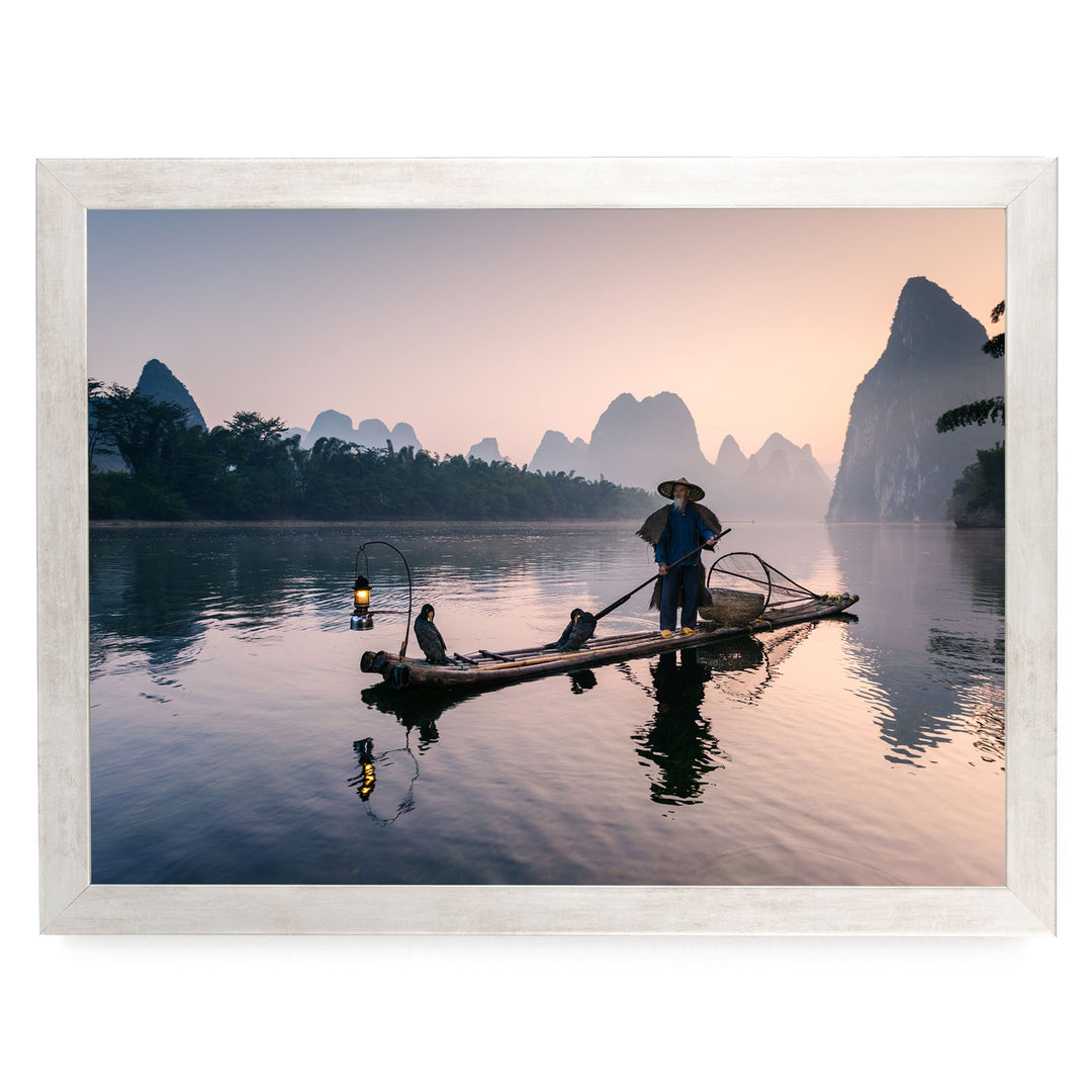 A person in a boat on a river at sunset, with mountains in the background.
