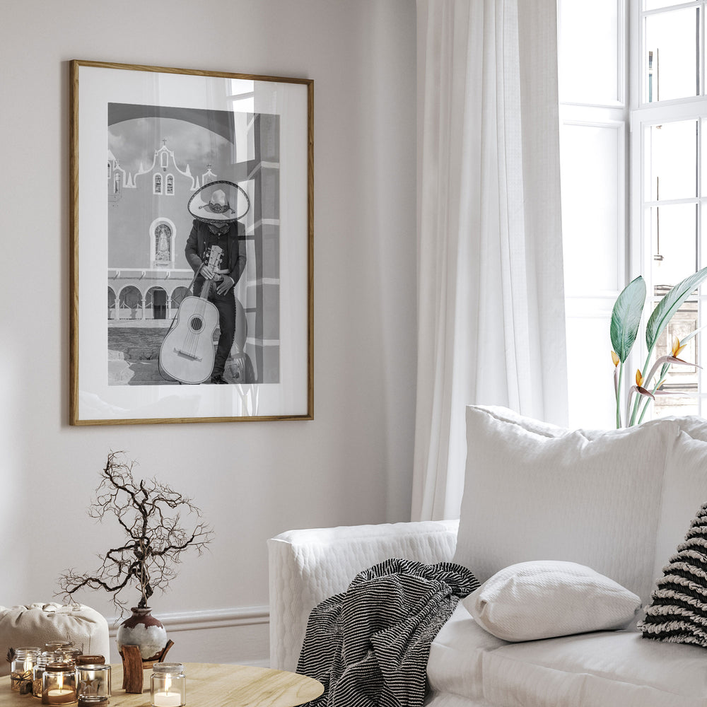 a cozy living room with a white sofa, a framed black and white photograph of a man playing a guitar, and a vase with dried branches on a coffee table.